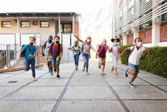 Group of diverse students wearing face masks running at elementary school. education back to school health safety during covid19 coronavirus pandemic.