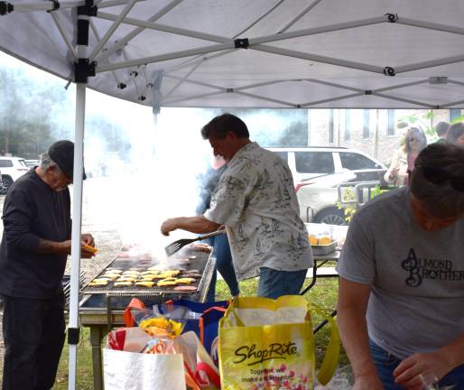 Church celebrates centennial CH3 Eduardo Nicheporuck, with spatula, grills burgers and hot dogs at the picnic. Kenny Mercado adds cheese and Eddie Dunn sets out buns.