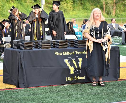 Kate Romeo, president of the Board of Education, waits beside the stacks of diplomas.