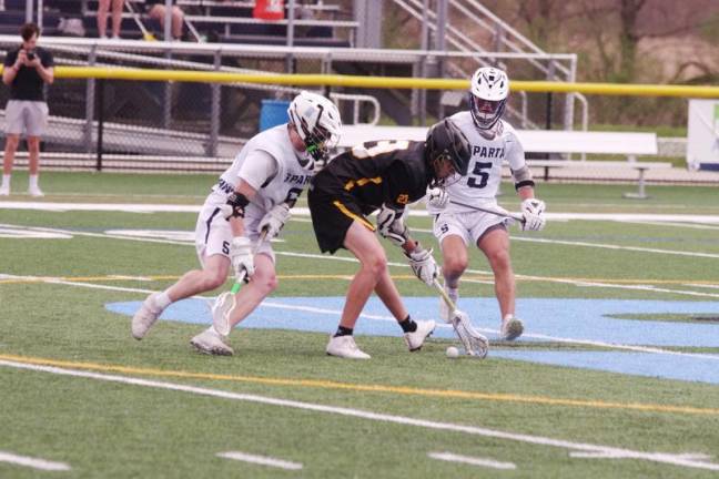 A West Milford Highlander attempts to scoop up the ball as two Sparta Spartans close in.