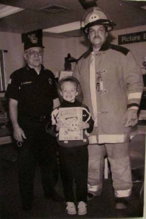 Photo courtesy of Ann Genader Fred Stewart, left, and Ron Dygos honored Alana Haight (then 6) as the West Milford Fire Company 6 coloring contest winner in 1995.