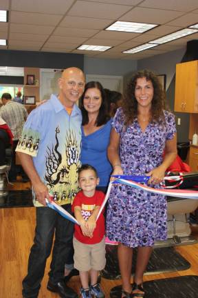 Celebrating the grand re-opening of Jimmy the Barber's at new location on Union Valley Road. West Milford's mayor, Bettina Bieri, cuts the ribbon to officially open the shop. Pictured here, left to right, owner Jimmy Thurstans, his wife Joan, Mayor Bieri and the Thurstans' grandson, Austen, helping out. Photo by Ginny Raue