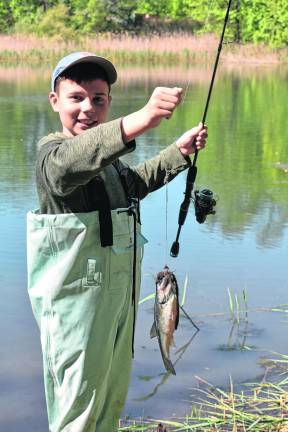 Young Evan with hip waders proudly displays his bass caught at the 7th annual West Milford Fishing Derby.