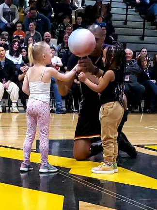 One of the Harlem Wizards helps two girls spin a basketball on their finger.