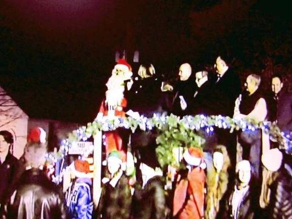 Santa Claus stands on a raised stand with West Milford officials at the Christmas tree lighting ceremony.