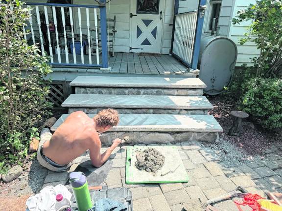 Mason Birkoff, a third-generation member of a stone/brick laying tradesmen family, restores porch steps on a West Milford home built about 175 years ago. Photo provided by Owen Ginder.
