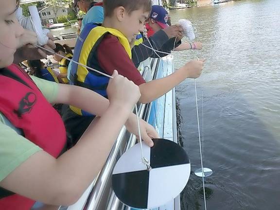 Guests aboard the Lake Hopatcong Floating Classroom take part in scientific experiments like water clarity testing with secchi disks.