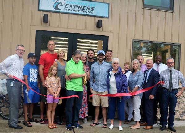Photo by Roger Gavan On Aug. 1, Warwick Supervisor Michael Sweeton (left), Mayor Michael Sweeton (right) and members of the Warwick Valley Chamber of Commerce joined owners John and Lynn Peruso (center), their relatives and friends to celebrate the official opening of their Express Laundry Center at 28 Forester Ave. in the Village of Warwick.