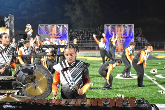 The band’s program, ‘High Voltage,’ is a sonic journey through a futuristic landscape, where pulsing rhythms drive a vibrant metropolis powered by a central energy source.
