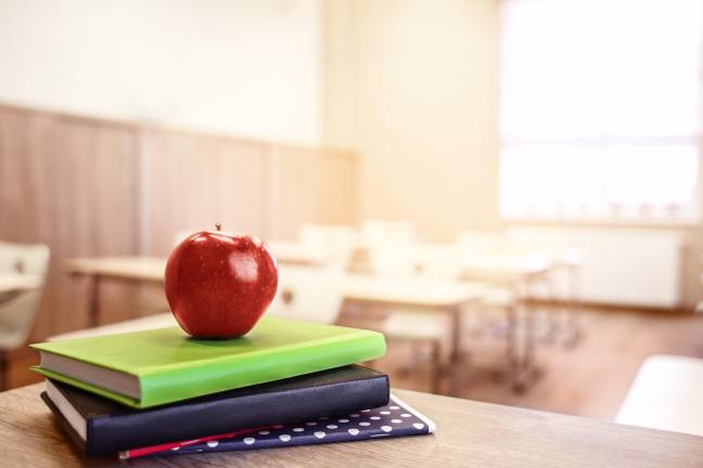 School teacher's desk with stack of books and apple