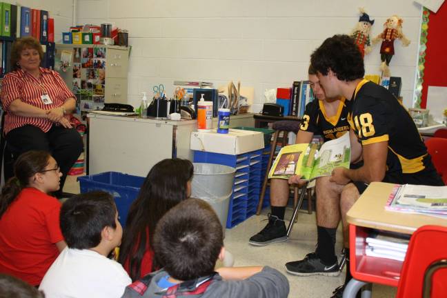 Theresa McCabe looks on as two of her former students, Dylan Walko, #18, and Thomas Murphy, #13, read to her students.