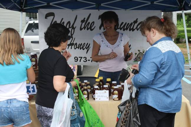 Customers take a taste of some local honey at the farmers market on Wednesday.