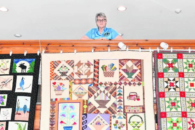 QT3 Meg Woznicki of Oak Ridge stands above quilts on display Saturday, March 16 at the West Milford Museum.