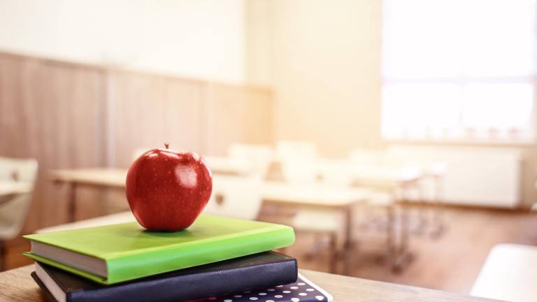 School teacher's desk with stack of books and apple