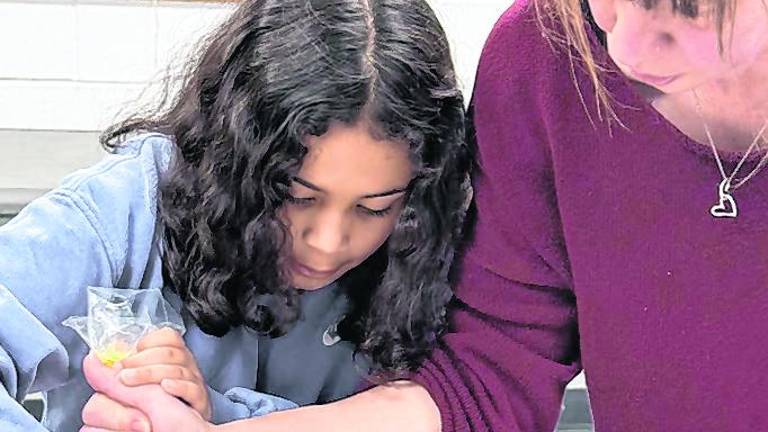 Xyra Valdez squeezes batter onto a baking pan while Marjory Yacca helps.